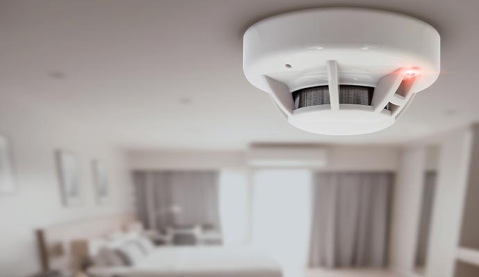 A white smoke and carbon monoxide detector mounted on a ceiling with a red indicator light active