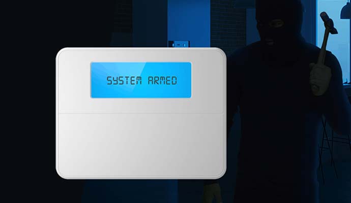 Burglar alarm keypad displaying system armed with intruder in background