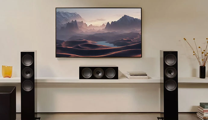 A premium home cinema setup featuring KEF R Series floorstanding speakers and a matching center channel speaker in Gloss Black