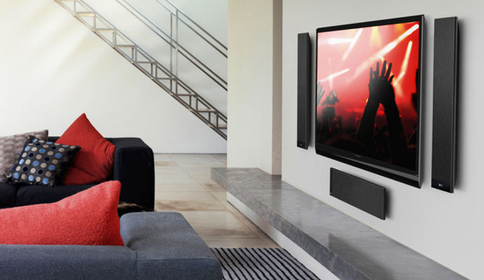 Three ultra-slim black KEF T Series speakers mounted to a white wall around a flat-screen TV
