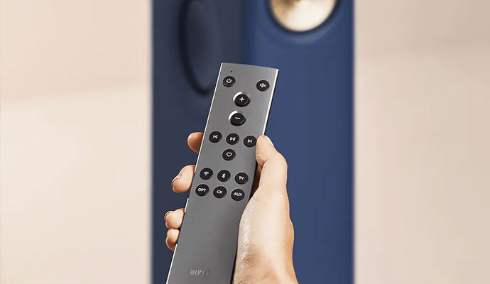 A close-up of a person' holding a sleek, grey KEF remote control