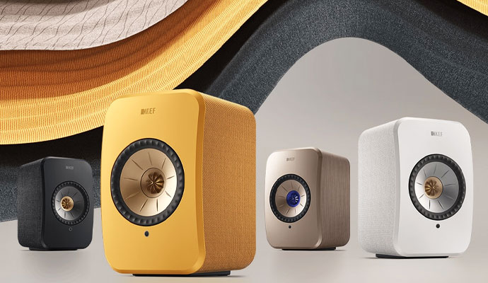 Four KEF LSX II wireless hi-fi speakers in Carbon Black, Ochre Yellow, Terra Cotta, and Mineral White
