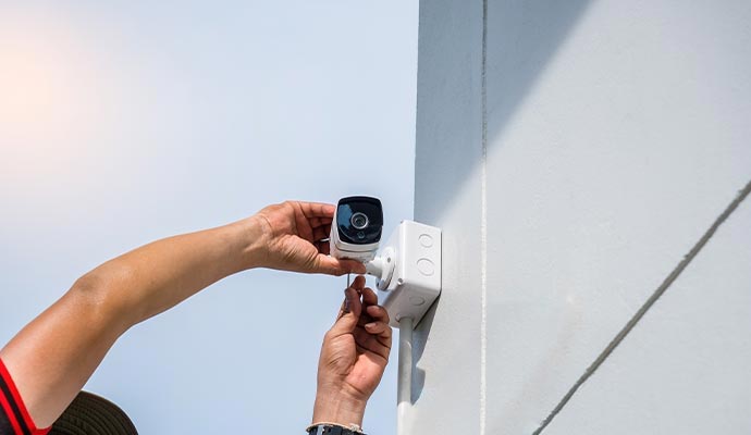 Technician installing a security camera on an outdoor wall.